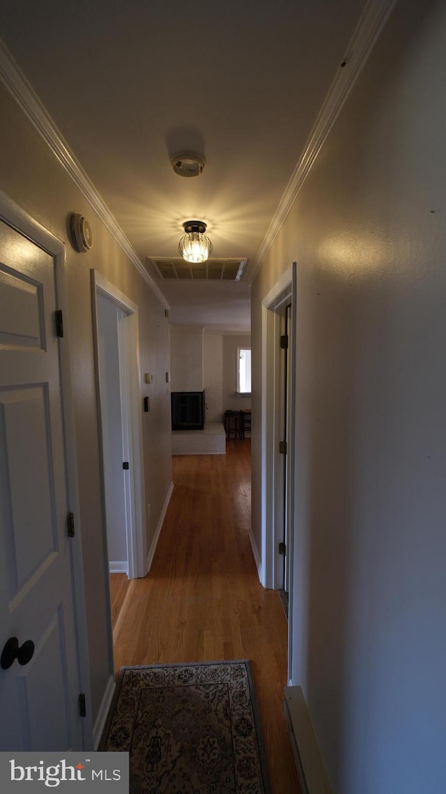 corridor with wood finished floors, ornamental molding, baseboards, and visible vents
