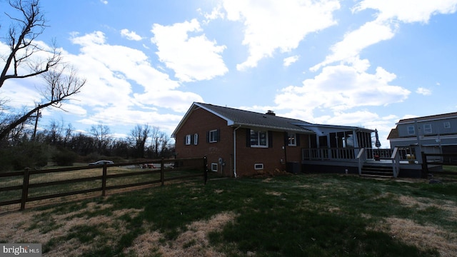 view of property exterior with cooling unit, fence, a deck, brick siding, and a yard