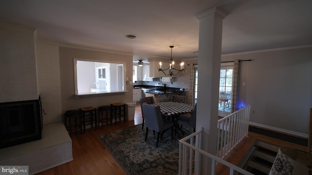 dining area featuring a brick fireplace, wood finished floors, ornamental molding, and an inviting chandelier