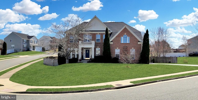 view of front of house with brick siding, fence, a residential view, a front yard, and a balcony