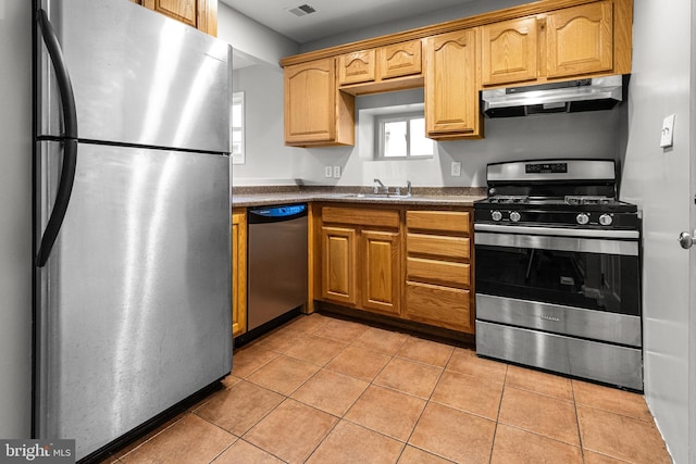 kitchen featuring dark countertops, under cabinet range hood, light tile patterned floors, appliances with stainless steel finishes, and a sink