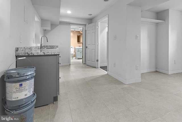 kitchen featuring light stone counters, recessed lighting, baseboards, and a sink