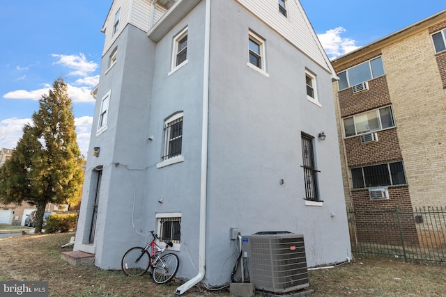 view of property exterior with cooling unit, fence, and stucco siding