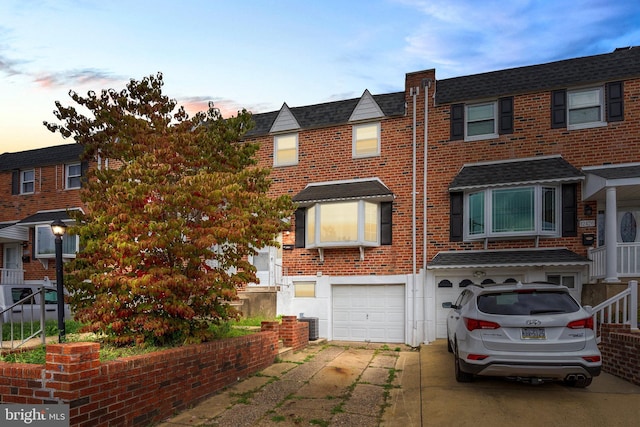 multi unit property with brick siding, an attached garage, concrete driveway, and a shingled roof