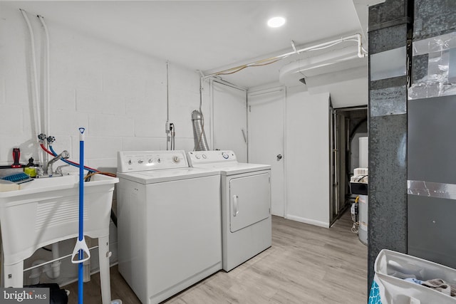 clothes washing area featuring light wood finished floors, laundry area, independent washer and dryer, concrete block wall, and a sink