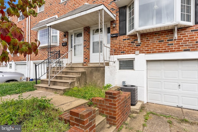 doorway to property with brick siding, an attached garage, and central AC