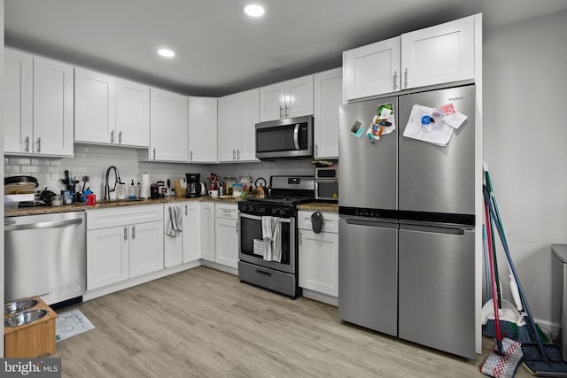 kitchen with decorative backsplash, white cabinetry, stainless steel appliances, and light wood-style floors