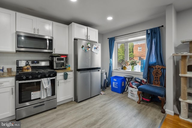 kitchen featuring white cabinetry, decorative backsplash, light wood finished floors, and stainless steel appliances