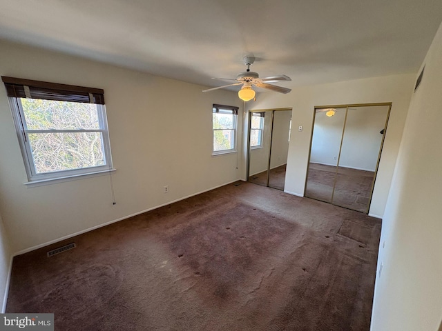 unfurnished bedroom with visible vents, ceiling fan, carpet, and multiple closets