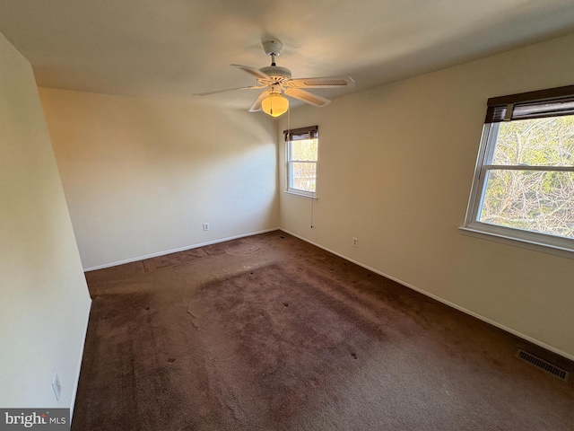 empty room with dark colored carpet, visible vents, baseboards, and ceiling fan