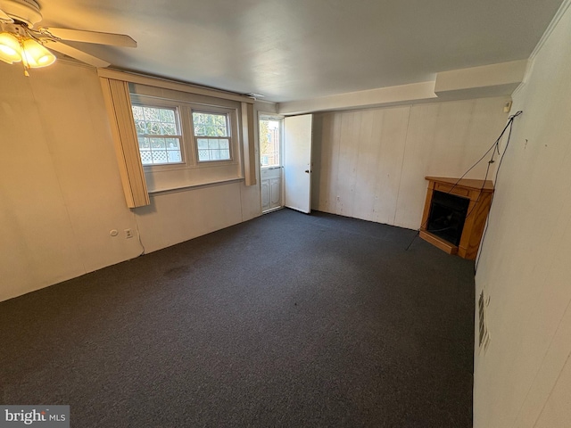 unfurnished living room with dark colored carpet, ceiling fan, and a fireplace