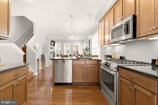 kitchen featuring stainless steel appliances, a peninsula, light wood-style flooring, dark countertops, and recessed lighting