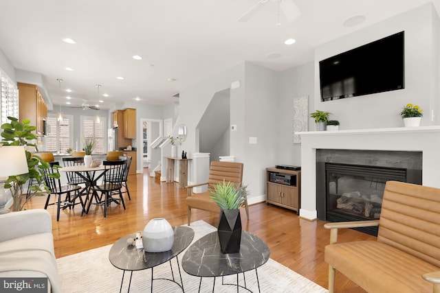 living room featuring a ceiling fan, a glass covered fireplace, light wood-style floors, baseboards, and recessed lighting