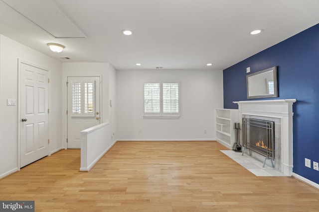 living area featuring a wealth of natural light, a fireplace with flush hearth, and light wood-style flooring