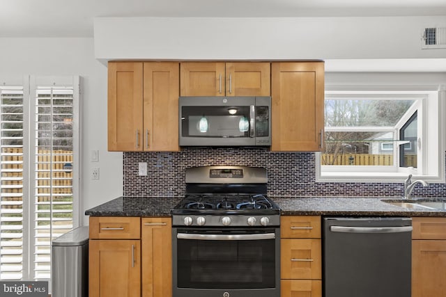 kitchen with tasteful backsplash, visible vents, dark stone countertops, stainless steel appliances, and a sink