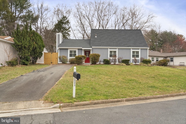 view of front of house featuring aphalt driveway, a chimney, a front yard, and a shingled roof