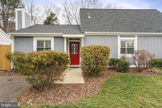 view of front of property featuring a chimney, a shingled roof, and a front lawn