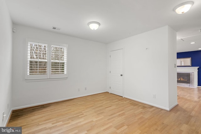 empty room with visible vents, a warm lit fireplace, baseboards, and wood finished floors