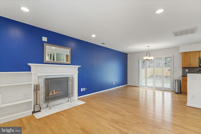 unfurnished living room featuring a tile fireplace, visible vents, light wood finished floors, and a chandelier