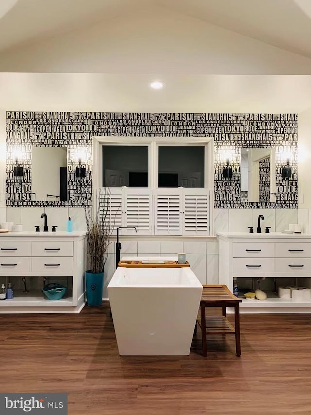 full bath featuring vaulted ceiling, two vanities, wood finished floors, and a sink