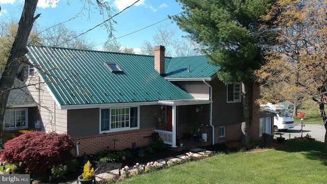 view of front of property featuring a front lawn, a porch, metal roof, brick siding, and a chimney