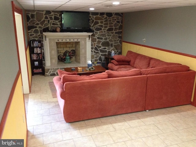 living room featuring a wainscoted wall, a fireplace with raised hearth, wood walls, and a drop ceiling