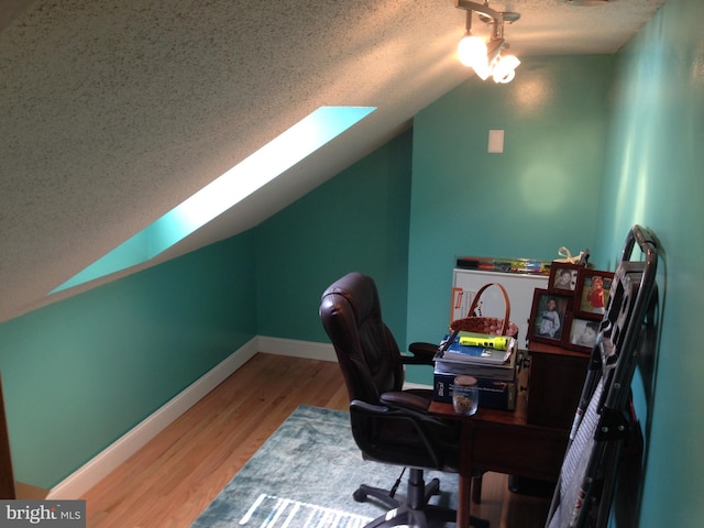 office area featuring vaulted ceiling with skylight, a textured ceiling, baseboards, and wood finished floors