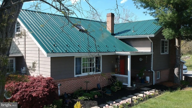 view of front of house with metal roof, brick siding, a porch, and a chimney