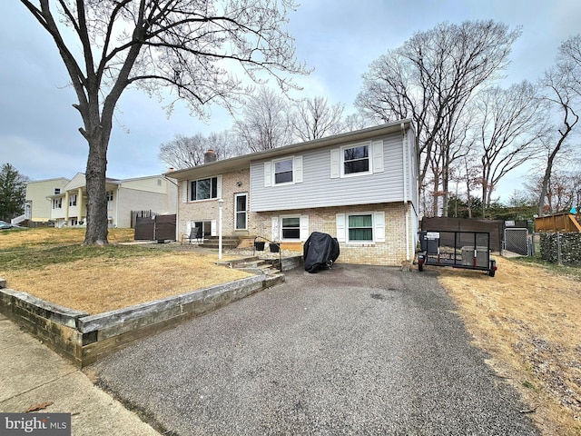 raised ranch with fence, a chimney, a front lawn, aphalt driveway, and brick siding