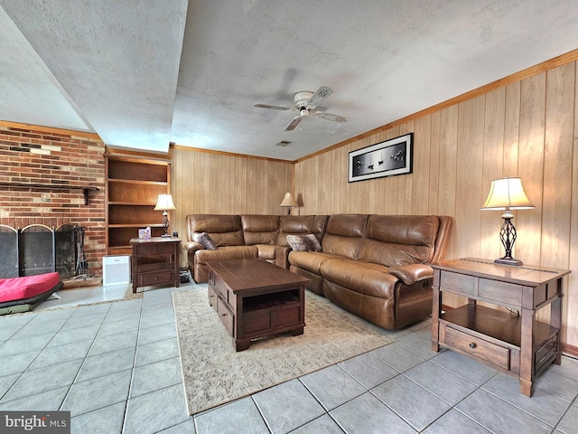 living room with wooden walls, built in features, light tile patterned floors, a ceiling fan, and a textured ceiling