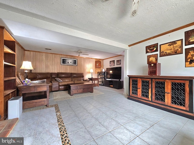 living area with a ceiling fan, a textured ceiling, wooden walls, light tile patterned flooring, and crown molding