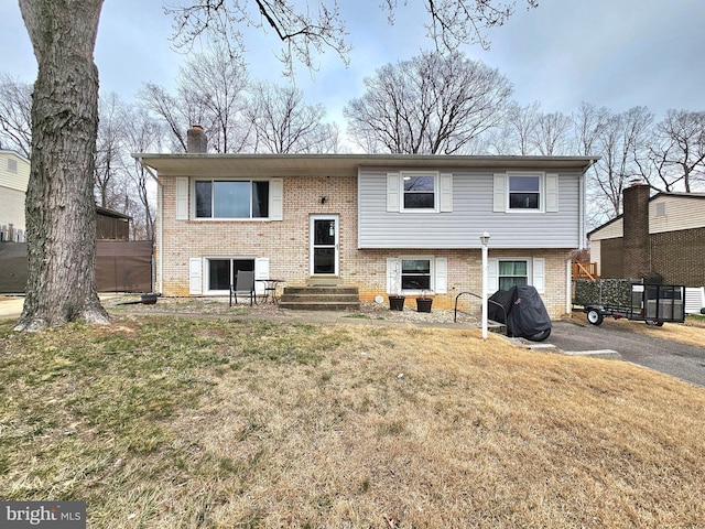 back of house with brick siding, entry steps, a chimney, and a yard