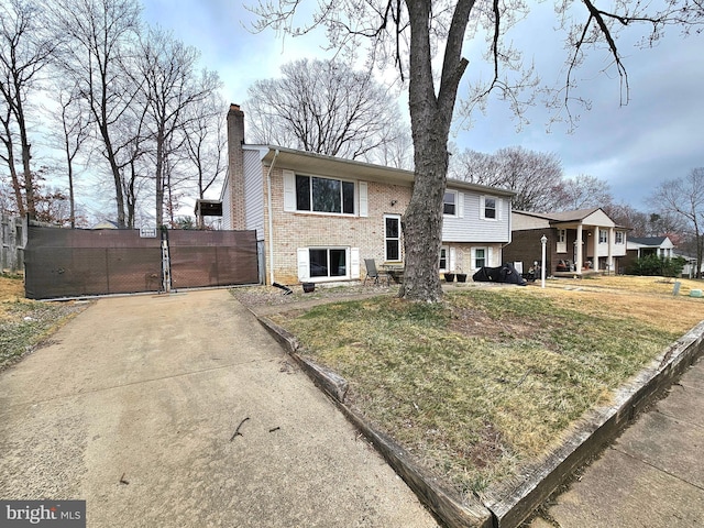 view of front of home with a front lawn, a gate, brick siding, and a chimney