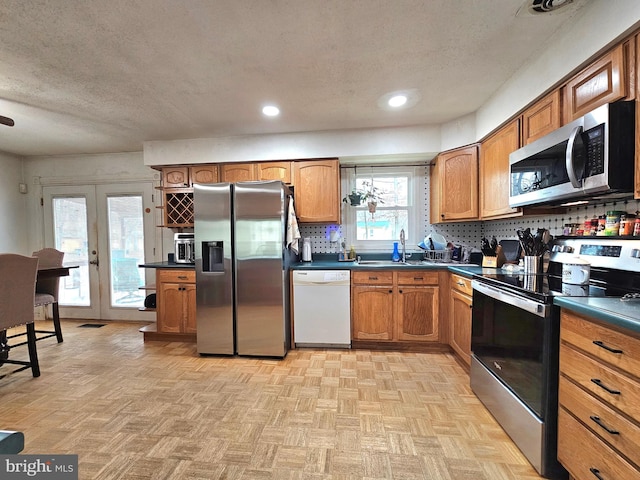 kitchen featuring a sink, stainless steel appliances, dark countertops, and brown cabinetry