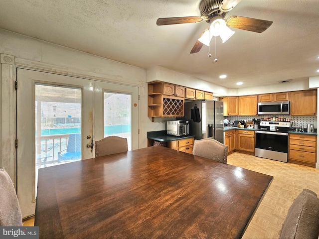 kitchen featuring open shelves, decorative backsplash, appliances with stainless steel finishes, a textured ceiling, and dark countertops