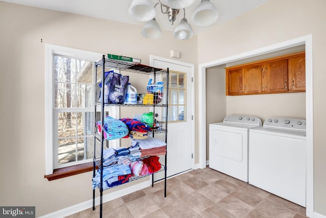 clothes washing area with a wealth of natural light, washer and dryer, cabinet space, and an inviting chandelier