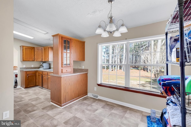 kitchen with light countertops, visible vents, a chandelier, lofted ceiling, and brown cabinetry
