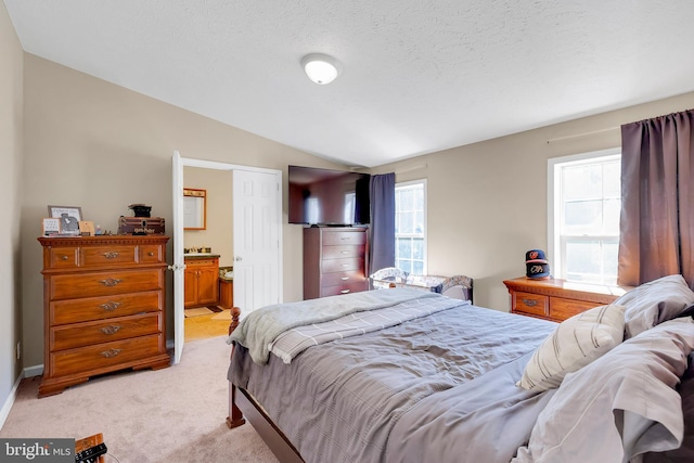 bedroom with ensuite bath, a textured ceiling, vaulted ceiling, and light colored carpet