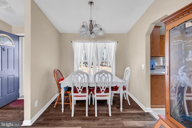 dining space with vaulted ceiling, wood finished floors, baseboards, arched walkways, and an inviting chandelier