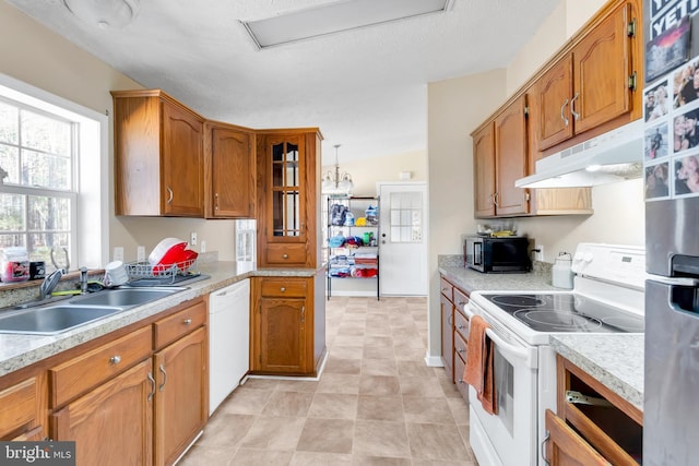 kitchen with light countertops, white appliances, under cabinet range hood, a sink, and brown cabinetry