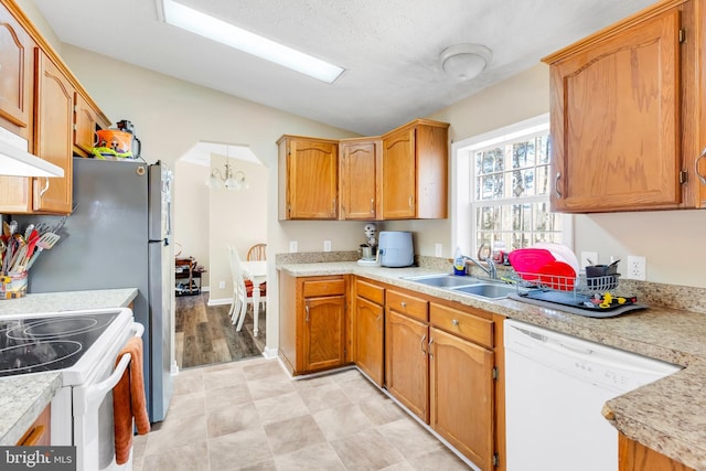 kitchen with light countertops, lofted ceiling, white appliances, under cabinet range hood, and a sink