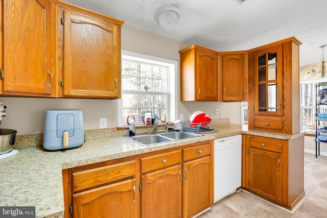 kitchen with dishwasher, light countertops, a sink, and brown cabinets