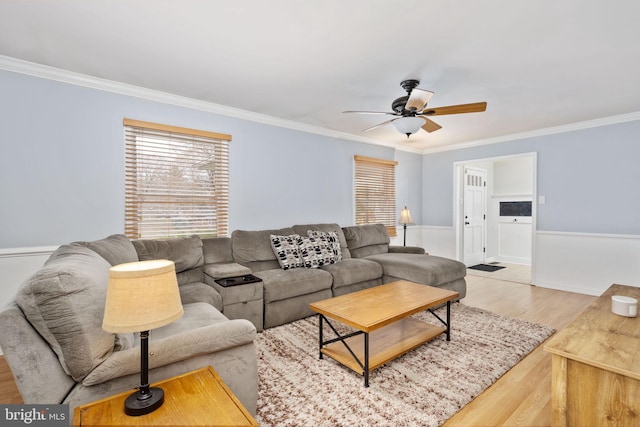 living room with wainscoting, a ceiling fan, light wood-style floors, and ornamental molding