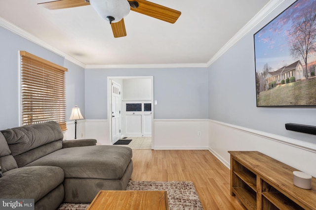 living room with ceiling fan, a wainscoted wall, wood finished floors, and crown molding