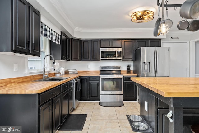 kitchen with dark cabinetry, stainless steel appliances, wood counters, and a sink