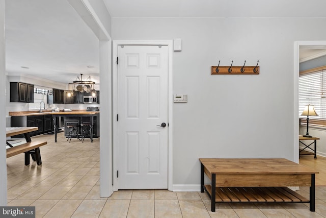 hall with light tile patterned floors, a chandelier, baseboards, and a sink