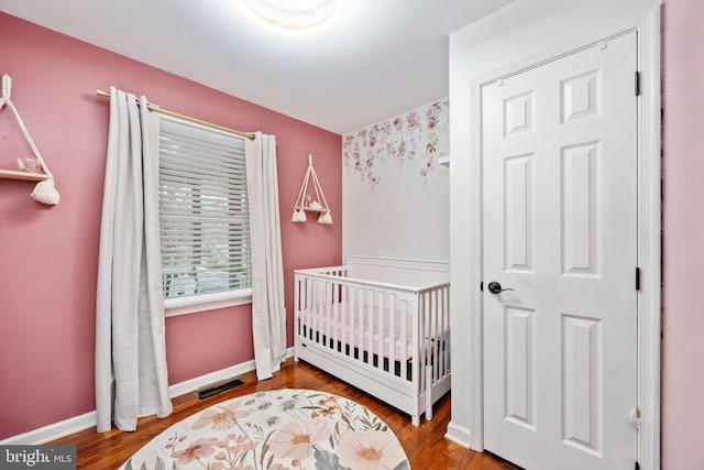 bedroom featuring visible vents, a crib, baseboards, and wood finished floors