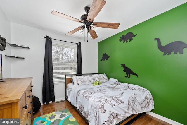 bedroom featuring ceiling fan, baseboards, wood finished floors, and an accent wall