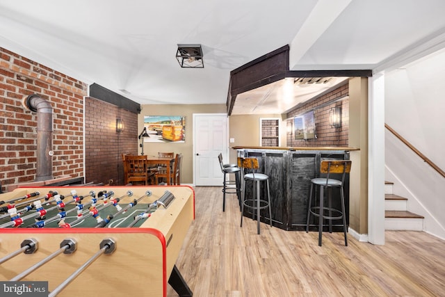 game room featuring a dry bar, brick wall, baseboards, and wood finished floors