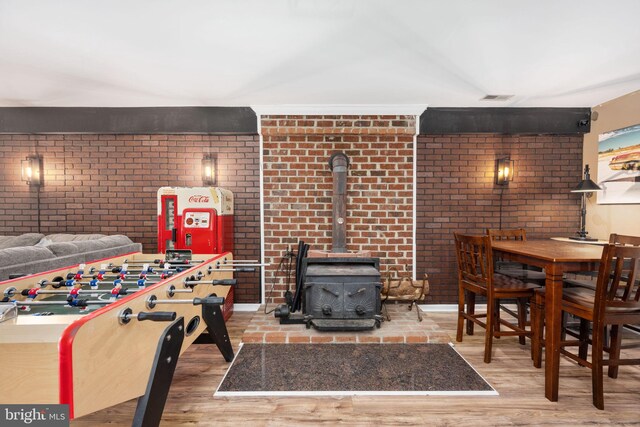 recreation room with a wood stove, wood finished floors, visible vents, and brick wall